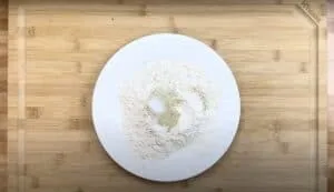 White plate with flour and spices on a wooden cutting board, ready for mixing. Ideal for cooking preparation visuals.